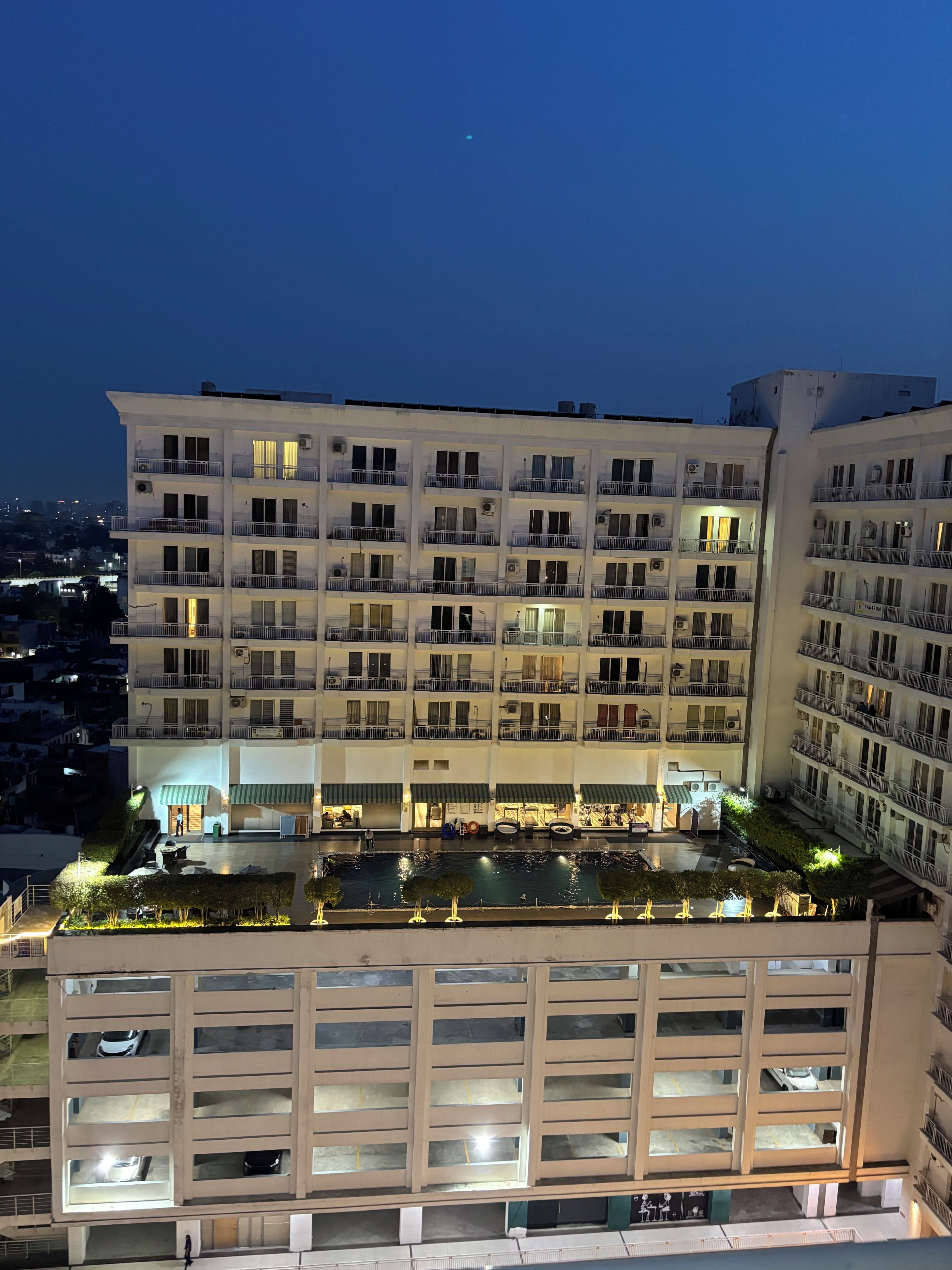 A multi-story hotel with balconies, a swimming pool, and a parking garage.
