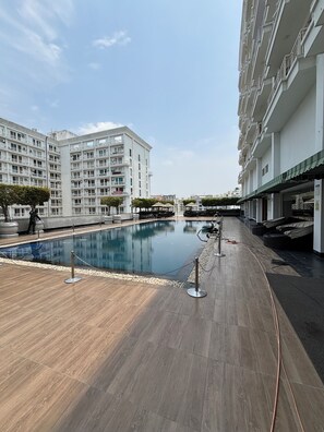 A swimming pool area with a wooden deck, surrounded by a white building with multiple balconies. - Privacy and comfort our first priority (Lucknow)
