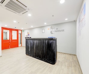 A reception area with a black counter, a red door, and a wall with the text 'OYO WHOUSE'. - Classic Hotel Rajyash Rise (Ahmedabad)