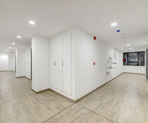 Un hall spacieux et bien éclairé, aux murs blancs et au plancher en bois, qui mène à une pièce dotée d’une grande fenêtre.