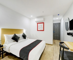 A hotel room with a bed, a desk, a chair, a door, and a wall-mounted TV. - Classic Hotel Rajyash Rise (Ahmedabad)