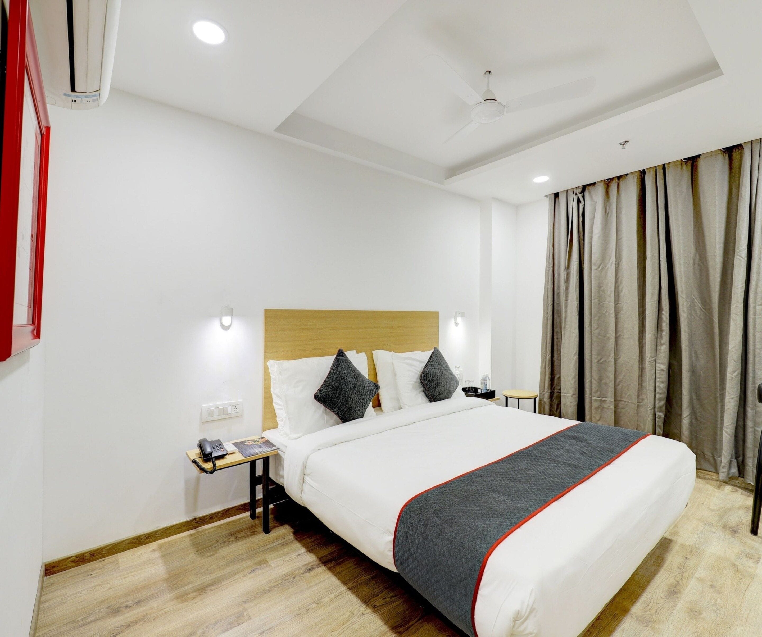 Una habitación de hotel con una cama, mesitas de noche, un teléfono y una ventana con cortinas.