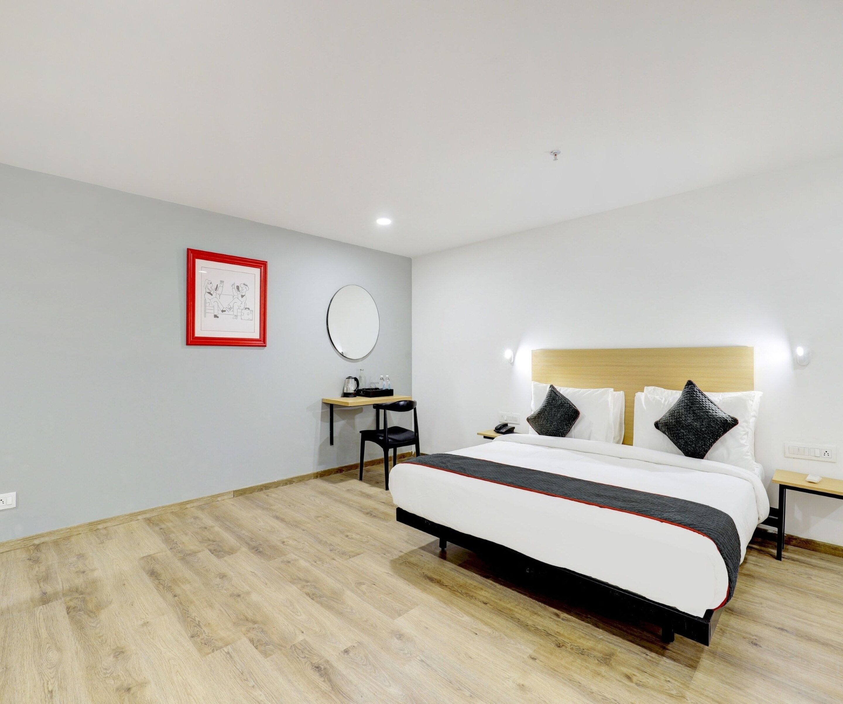 A hotel room with a large bed, a desk, a chair, a round mirror, and a framed picture on the wall.