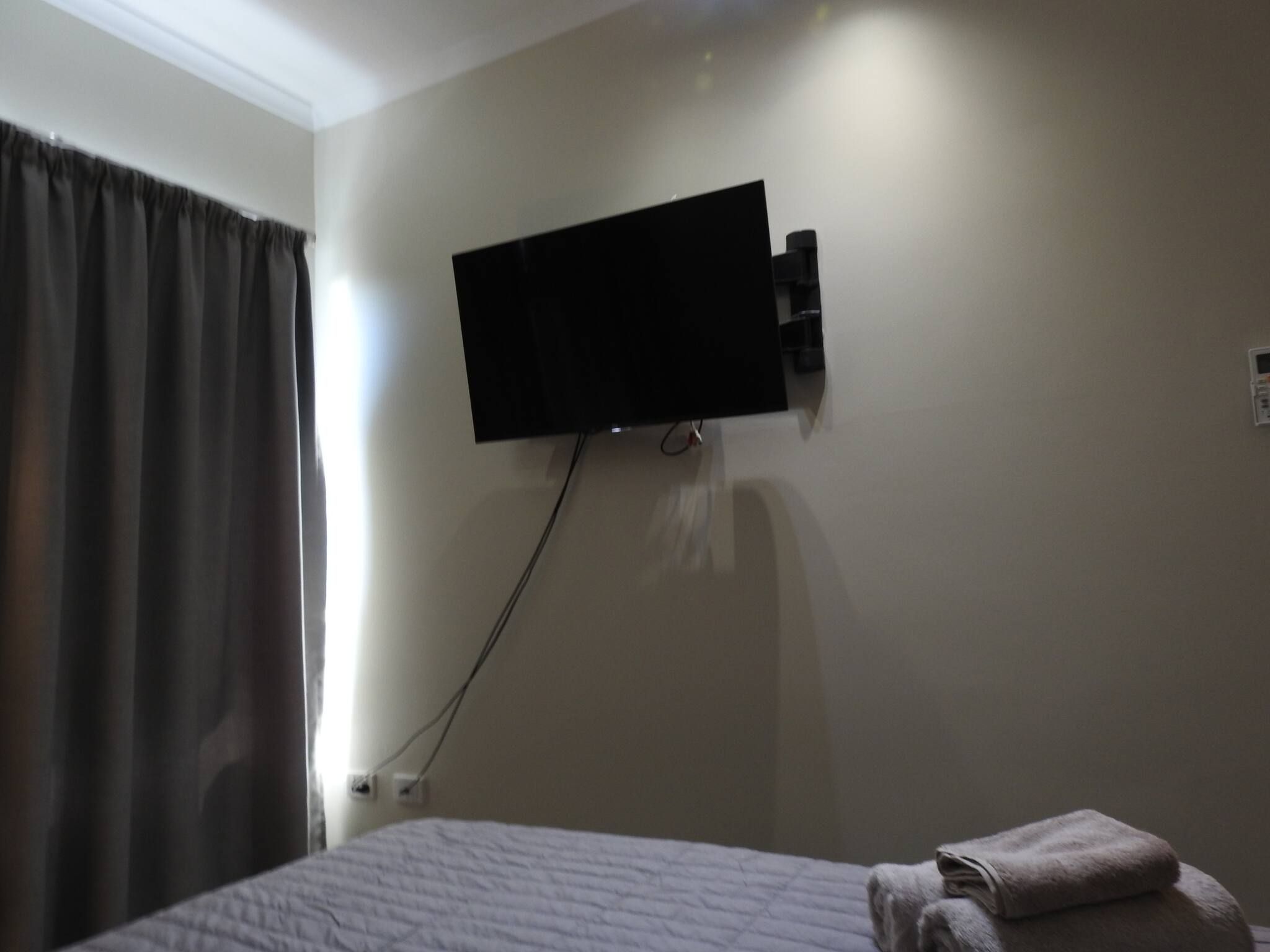 Une chambre d’hôtel avec un lit, un téléviseur fixé au mur et une fenêtre avec des rideaux.
