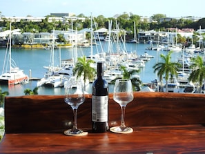 A bottle of wine and two glasses on a wooden table with a marina view in the background. - Luxury Living in Cullen Bay (Darwin City)