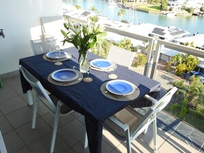 A dining table set with blue plates, a vase of flowers, and a glass of water on a balcony overlooking a marina. - Luxury Living in Cullen Bay (Darwin City)