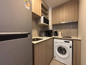 A compact kitchen with a refrigerator, microwave, coffee maker, and a washing machine. - The Base Rise Condo Phuket Middle of The Island (Tambon Wichit)