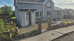 A two-story house with a grey exterior, a front door, and a small porch area. - Cottage on the hillx (Ballon)