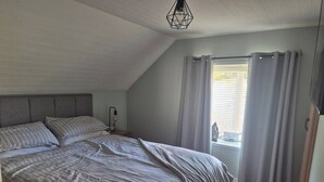A bedroom with a large bed, a nightstand, a lamp, and a window with curtains. - Cottage on the hillx (Ballon)