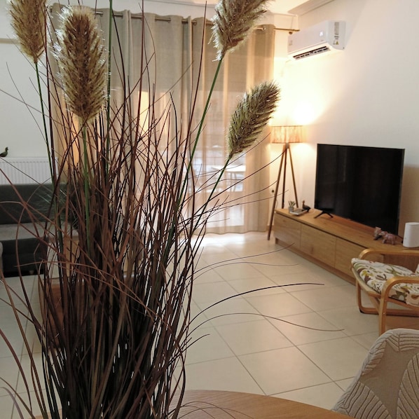 Een woonkamer met een grote plant, een bank, een televisie en een lamp.