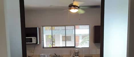 A kitchen with a microwave, coffee maker, and a window with blinds.