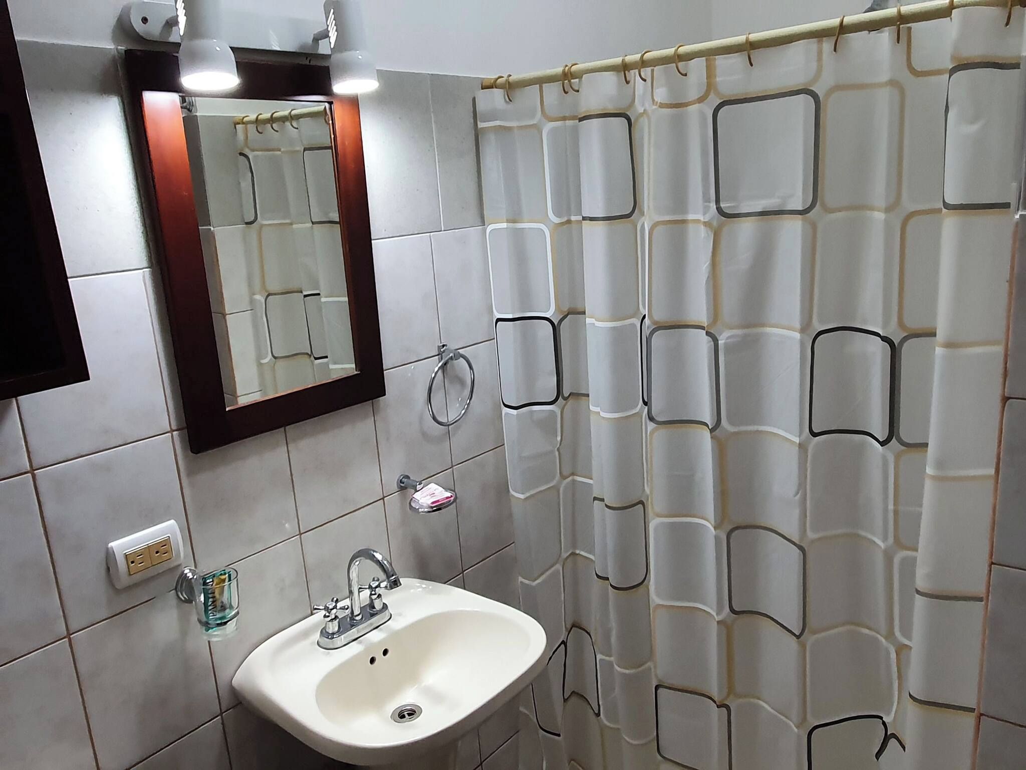 A bathroom with a white sink, a mirror, and a shower curtain with a geometric pattern.