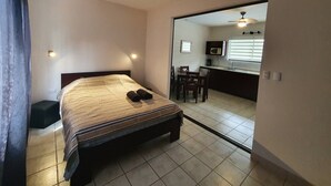 Una camera da letto con un letto, un comodino, una sedia e vista su una zona cucina.