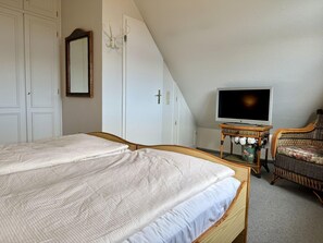 A bedroom with a bed, a television, a chair, and a mirror. - SyltRuhe - 2-room apartment for 4 people with a balcony, parking space, and Wi-Fi. Pet (Sylt)