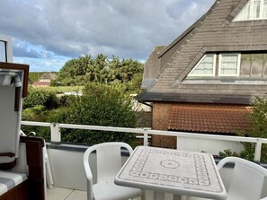 A balcony with a table and chairs, overlooking a residential area with houses and trees. - SyltRuhe - 2-room apartment for 4 people with a balcony, parking space, and Wi-Fi. Pet (Sylt)