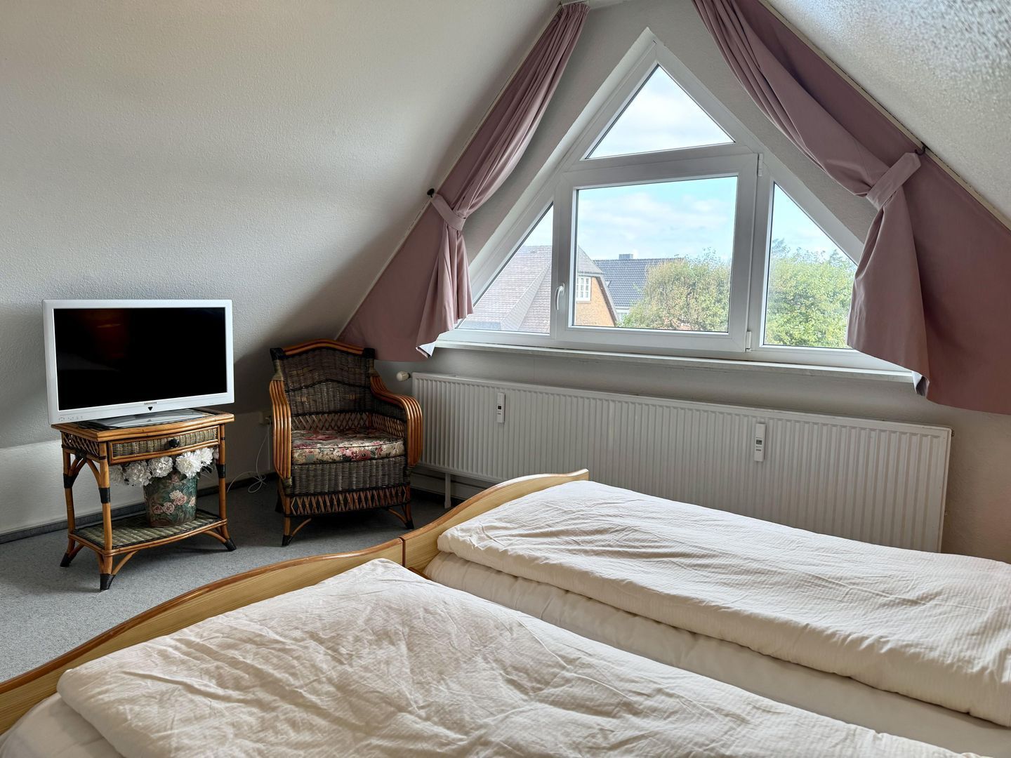 A bedroom with a TV on a stand, a chair, and a window with curtains.