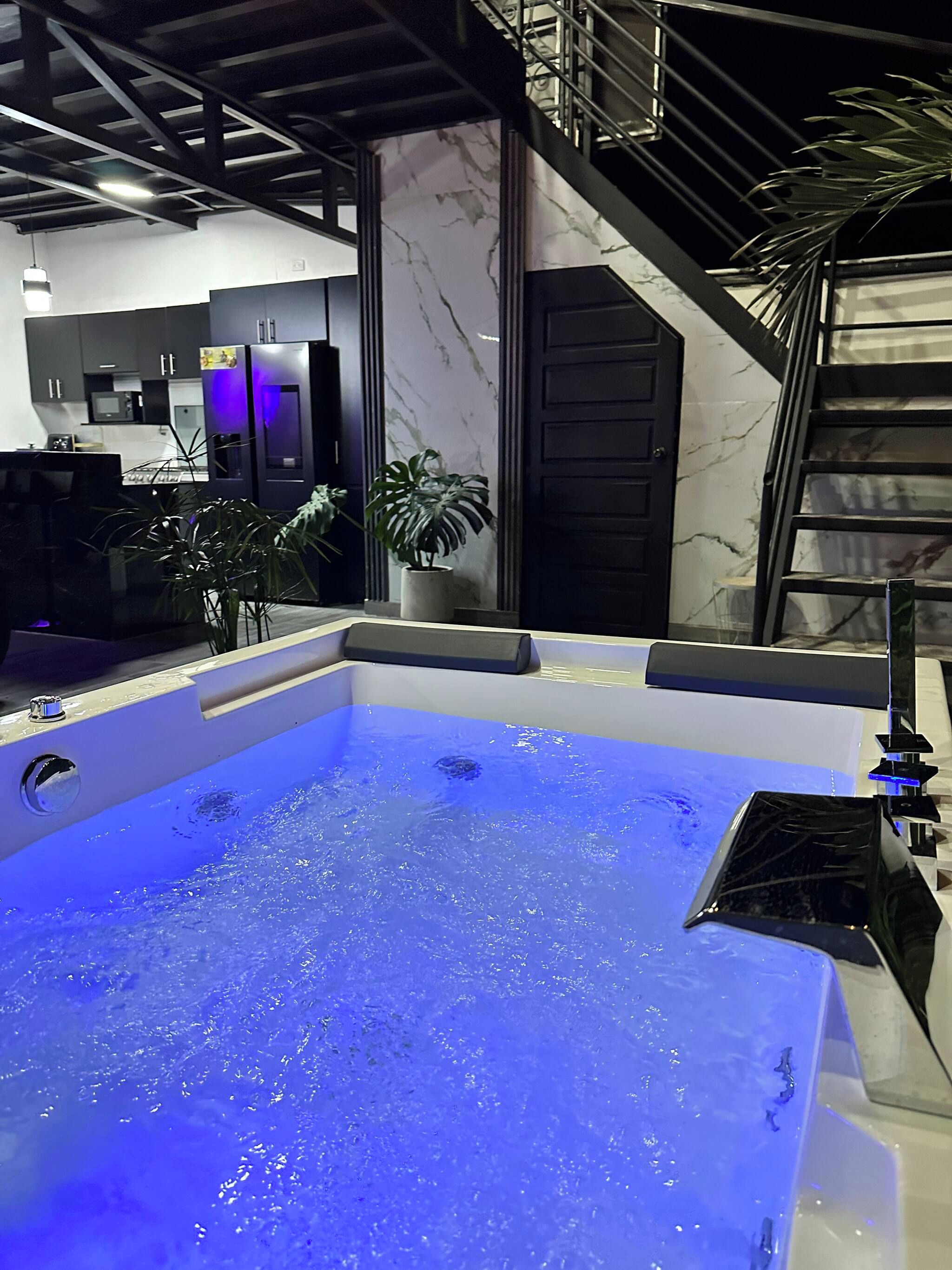 A modern bathroom with a large bathtub, a staircase, and a potted plant.