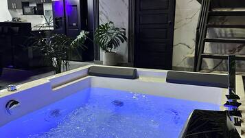 A modern bathroom with a large bathtub, a staircase, and a potted plant.