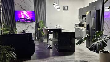 A modern kitchen with a built-in microwave, refrigerator, and stove. There is a dining area with a bar stool and a TV displaying a fire.