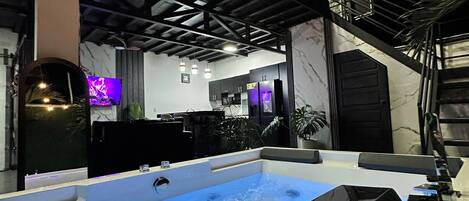 A modern indoor swimming pool with a clear water surface, surrounded by a high ceiling with exposed beams and pendant lighting.