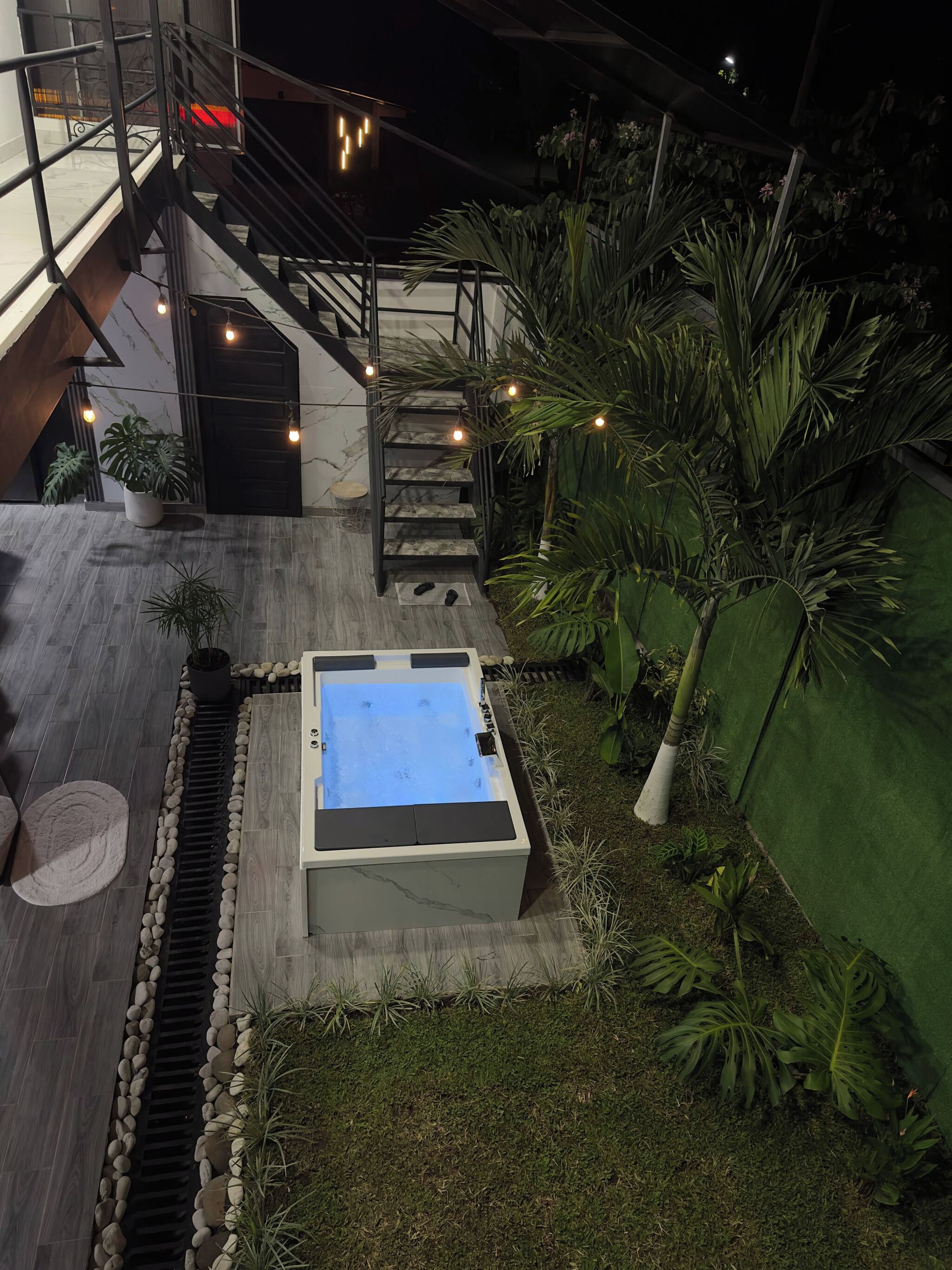 A rooftop pool with a stone border, a staircase, and surrounding greenery.