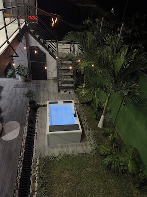 A rooftop pool with a stone border, a staircase, and surrounding greenery.