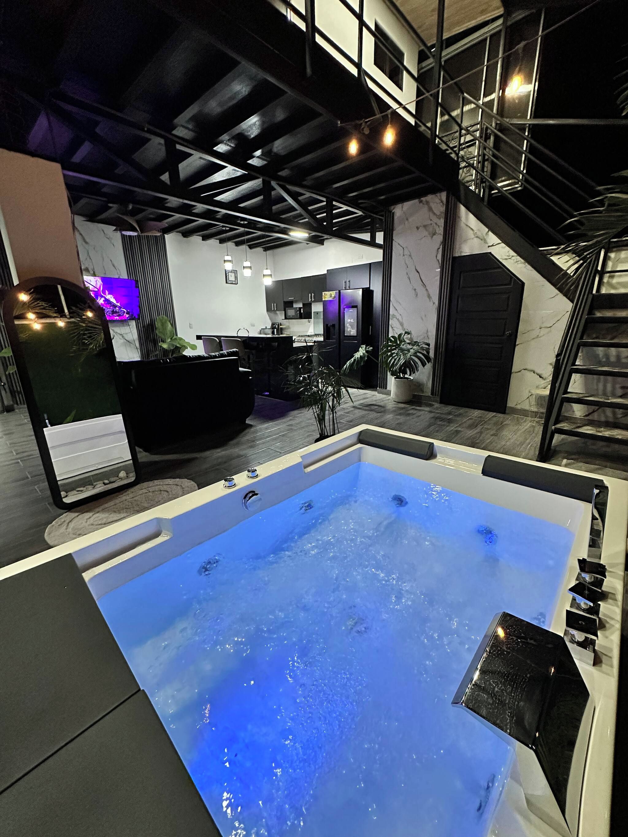 A modern interior with a hot tub, a kitchen area, and a staircase.