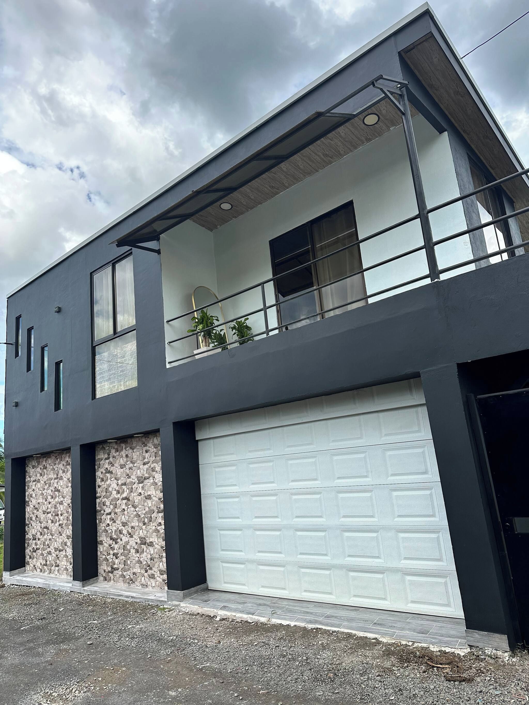 A modern two-story house with a garage, stone facade, and a balcony with plants.