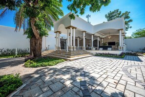A modern building with a covered outdoor area, stone paving, and a large tree. - The Palace 10BR Villa Luxury Pool, Jacuzzi, Resort Style Bar (Jaco)