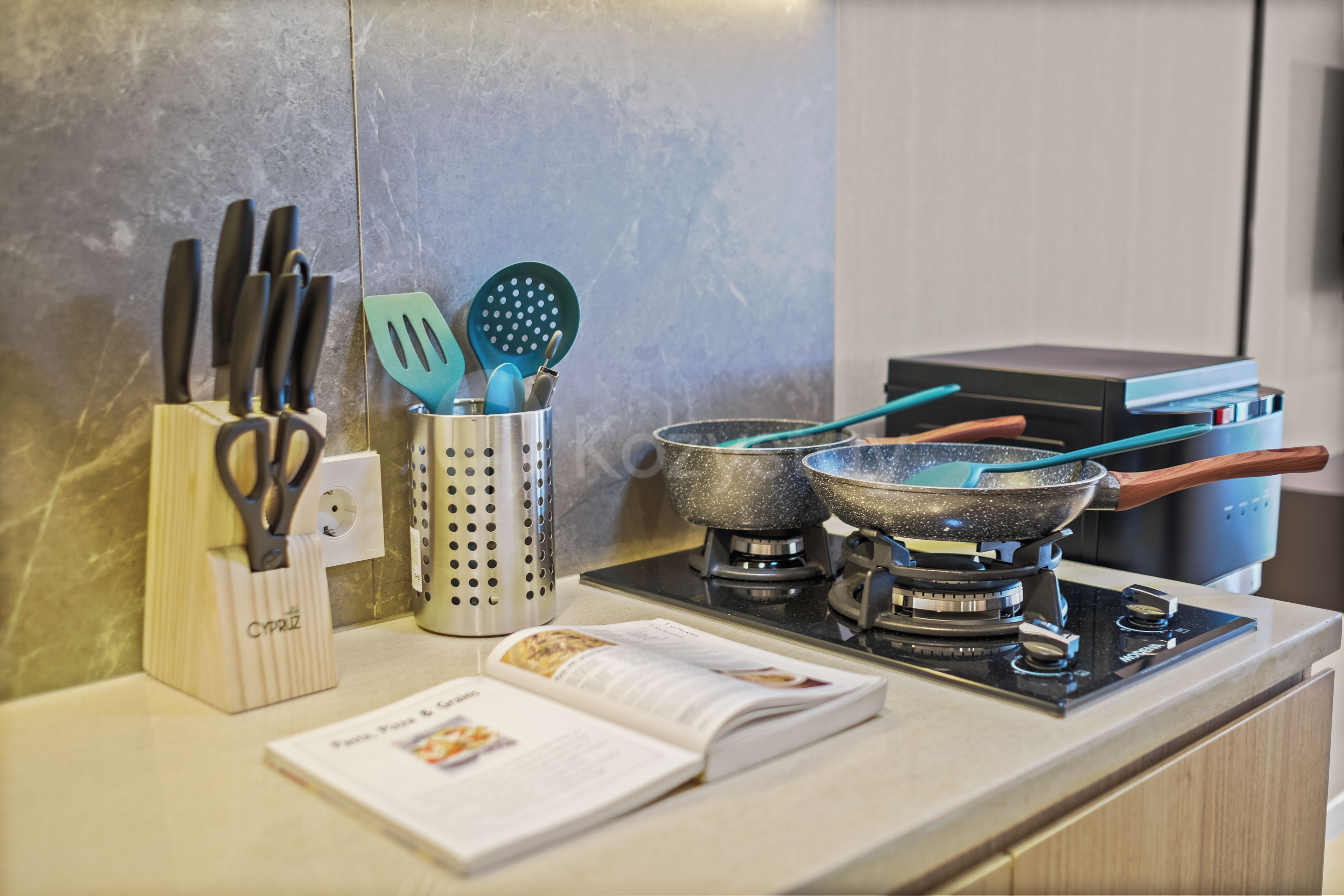 A kitchen counter with cooking utensils, a cookbook, and a stove.