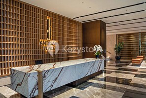 A reception area with a marble reception desk, wooden panel wall, and a potted plant. - Eslin by Kozystay - Cilandak (South Jakarta)