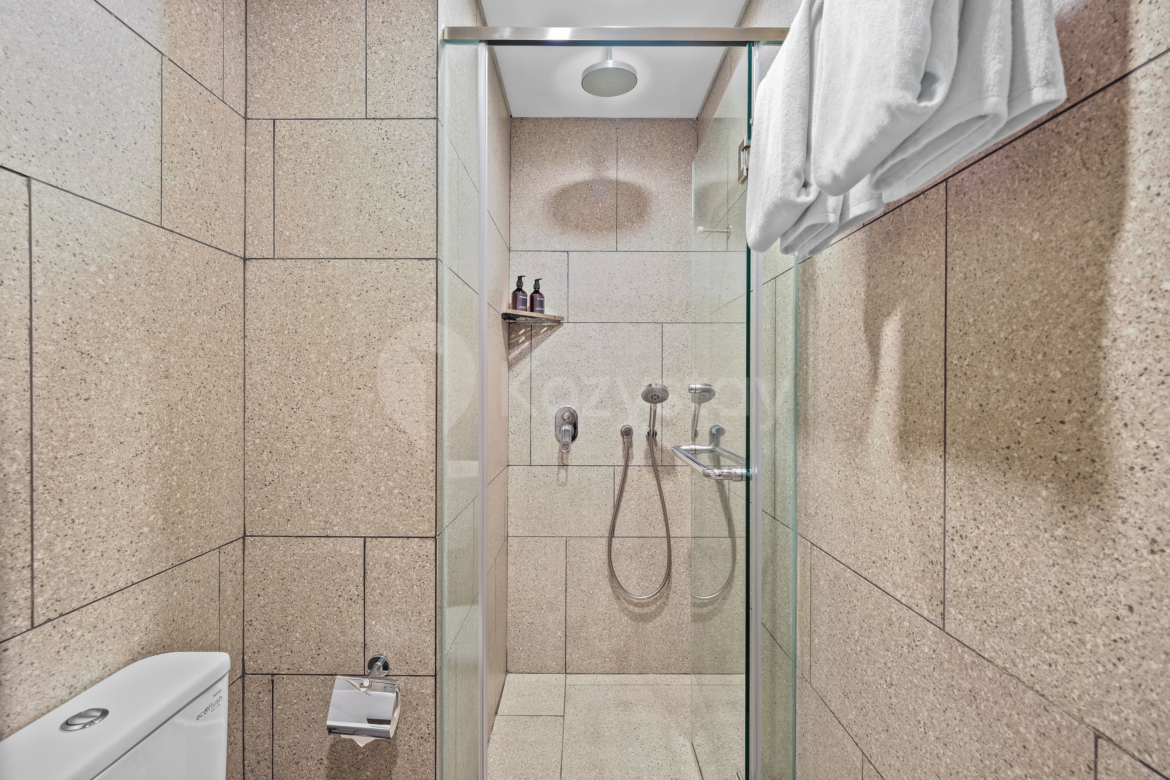Ein modernes Badezimmer mit einer gläsernen Duschkabine, einer weißen Toilette und einem Handtuch an der Wand.