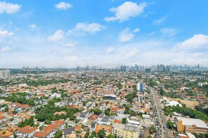 Paesaggio urbano con edifici residenziali e commerciali, cielo sereno e una linea dell'orizzonte cittadina in lontananza.