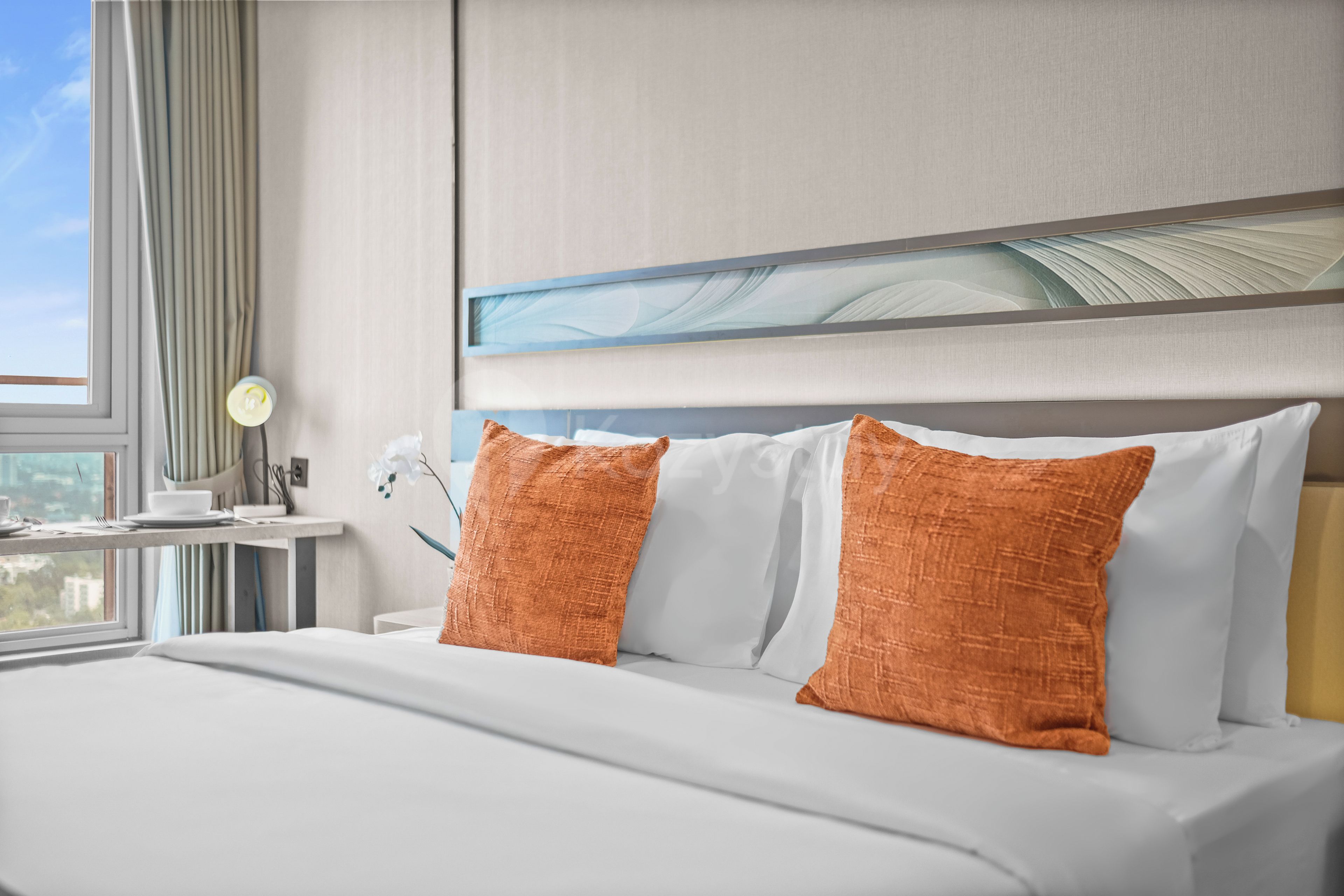 A hotel room with a bed, a nightstand, a lamp, and a window with curtains.