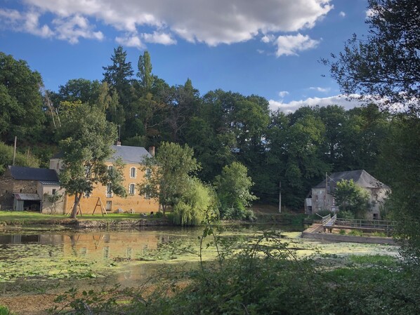 Um edifício histórico com um lago em frente, cercado por árvores e um céu claro.