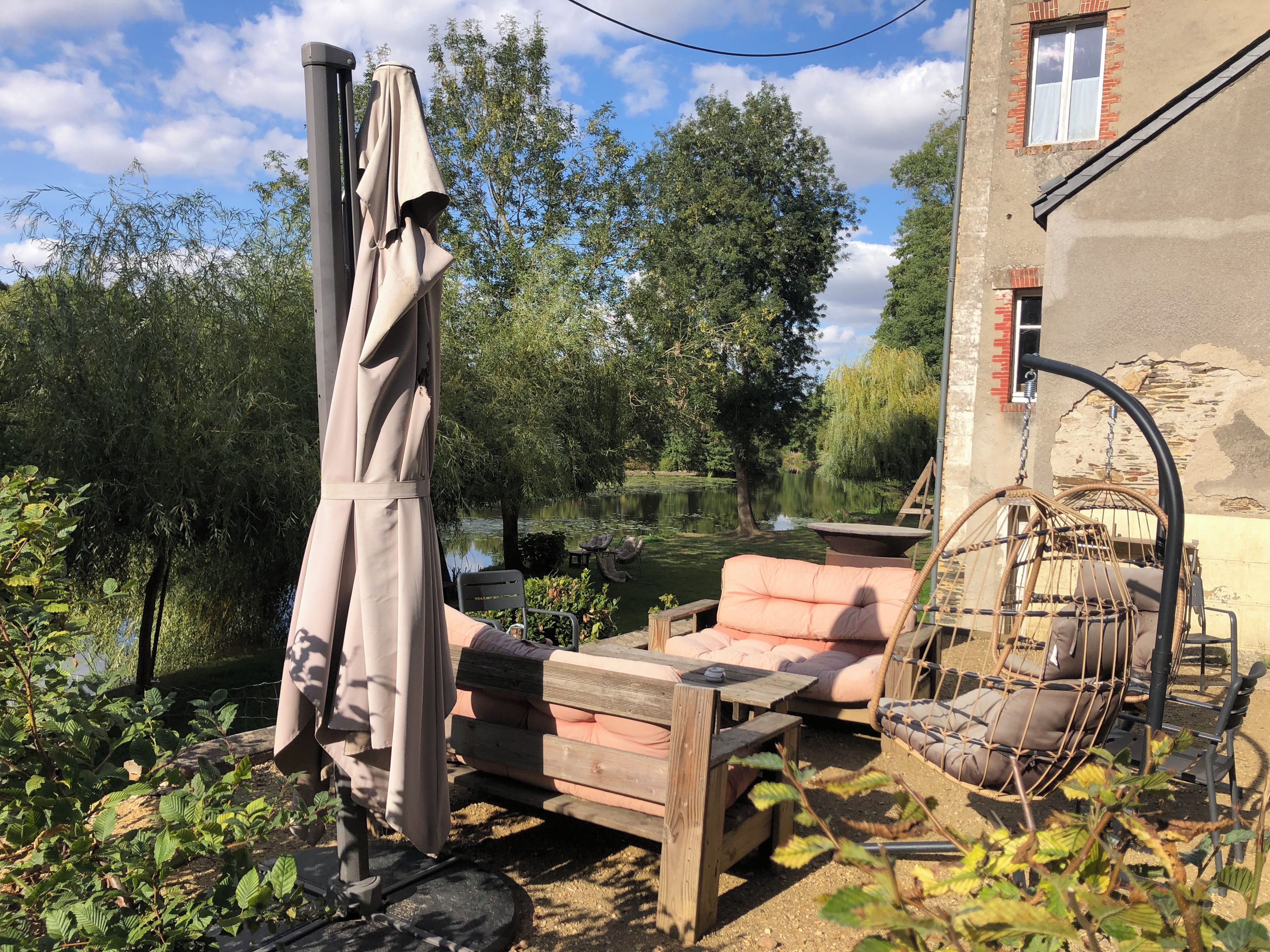 Une terrasse avec une table et des chaises en bois, un fauteuil suspendu et un parasol.