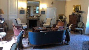Ein traditionell eingerichtetes Wohnzimmer mit Kamin, mehreren Sesseln, einer Couch und einem Spiegel.