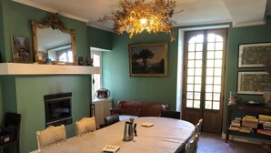 Ein Esszimmer mit rundem Tisch, Stühlen, einer Kandelaber, einem Kamin und einem Bücherregal.