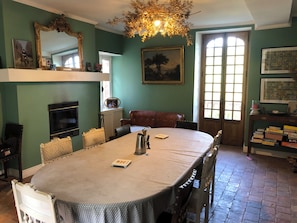 Uma sala de jantar com mesa redonda, cadeiras, lustre, lareira e estante de livros.
