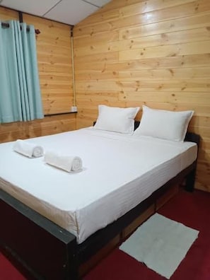 Un lit simple avec du linge de lit blanc et des oreillers, une tête de lit en bois et un sol recouvert d’une moquette rouge.