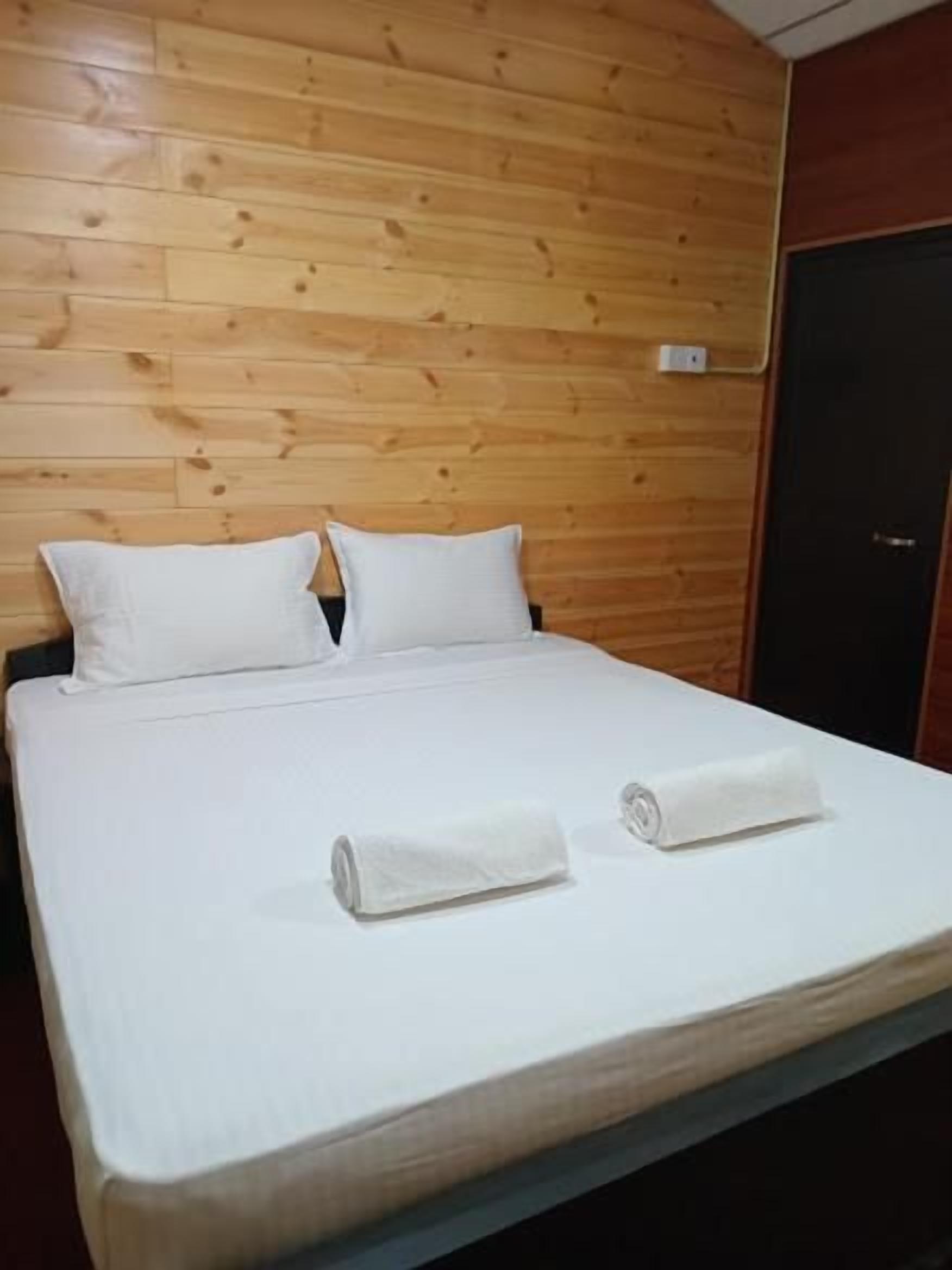 A bed with white linens and pillows, a wooden headboard, and a dark-colored wardrobe.