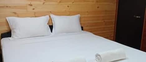 A bed with white linens and pillows, a wooden headboard, and a dark-colored wardrobe.