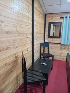 Una habitación con pared de madera, una mesa negra con dos sillas, alfombra roja y un espejo en la pared.