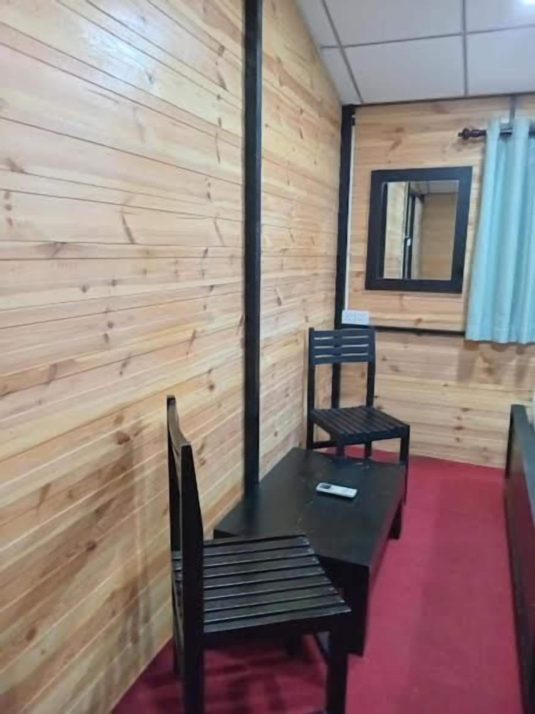 A room with wooden panel walls, a red carpet, a black table with chairs, and a mirror on the wall.