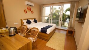 A hotel room with a bed, a desk, a chair, a TV, and a balcony with a view of palm trees. - Narayani Vista Riverside Resort  (Kawasoti)
