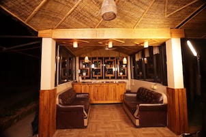 Una zona de bar con mobiliario de madera, techo de paja y plantas en macetas.