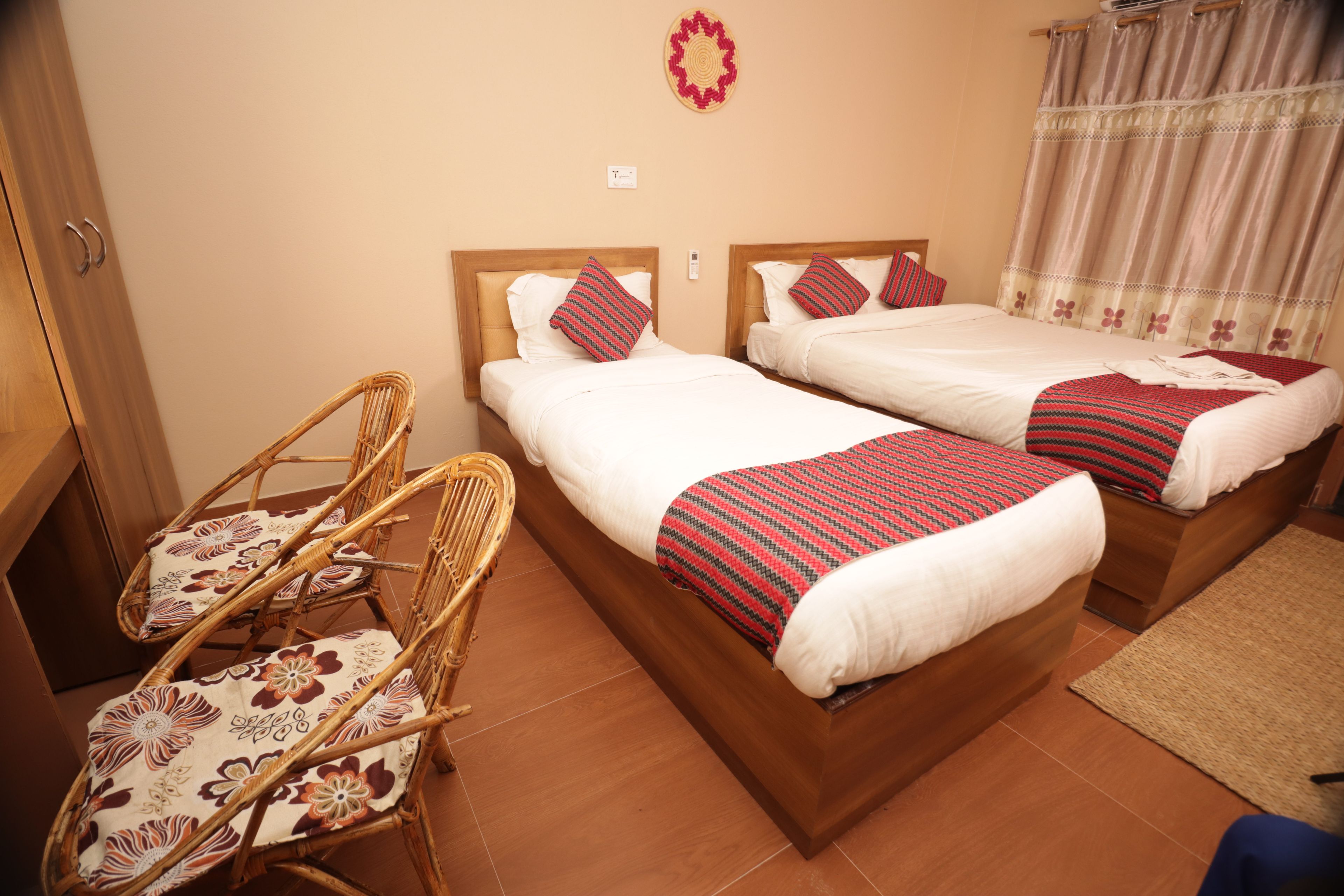 Habitación de hotel con dos camas, cabecera de madera, una silla de mimbre y una alfombra pequeña.