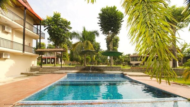 A swimming pool with a tiled edge, surrounded by a building with balconies and a covered seating area. - Narayani Vista Riverside Resort  (Kawasoti)