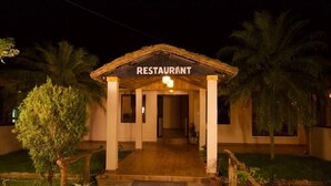 A restaurant with a thatched roof entrance, palm trees, and a paved walkway. - Narayani Vista Riverside Resort  (Kawasoti)