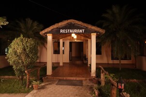 Un restaurante con entrada de techo de paja, un camino pavimentado y plantas en macetas.